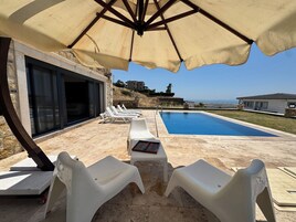 Área da piscina com espreguiçadeiras, guarda-sol e vista para o mar.