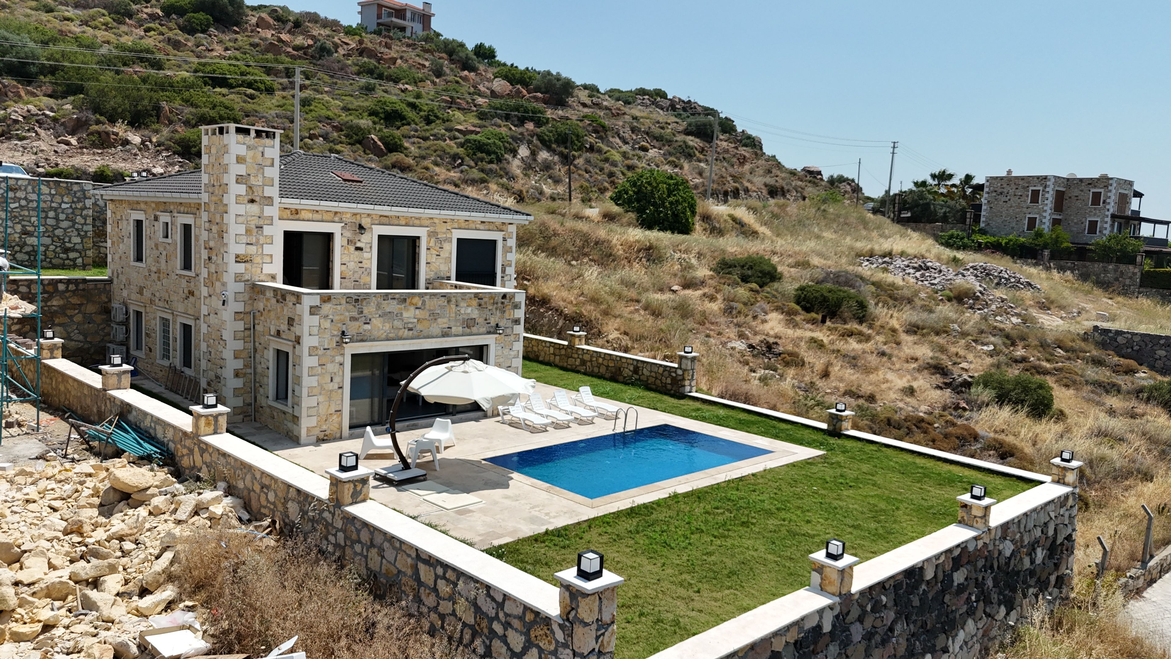 Une maison en pierre avec une piscine, entourée d’un mur de pierre et d’une pelouse verdoyante.