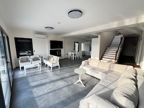 A spacious living area with a sofa, chairs, a dining table, and a staircase. - Foça Taş Villa (foça)