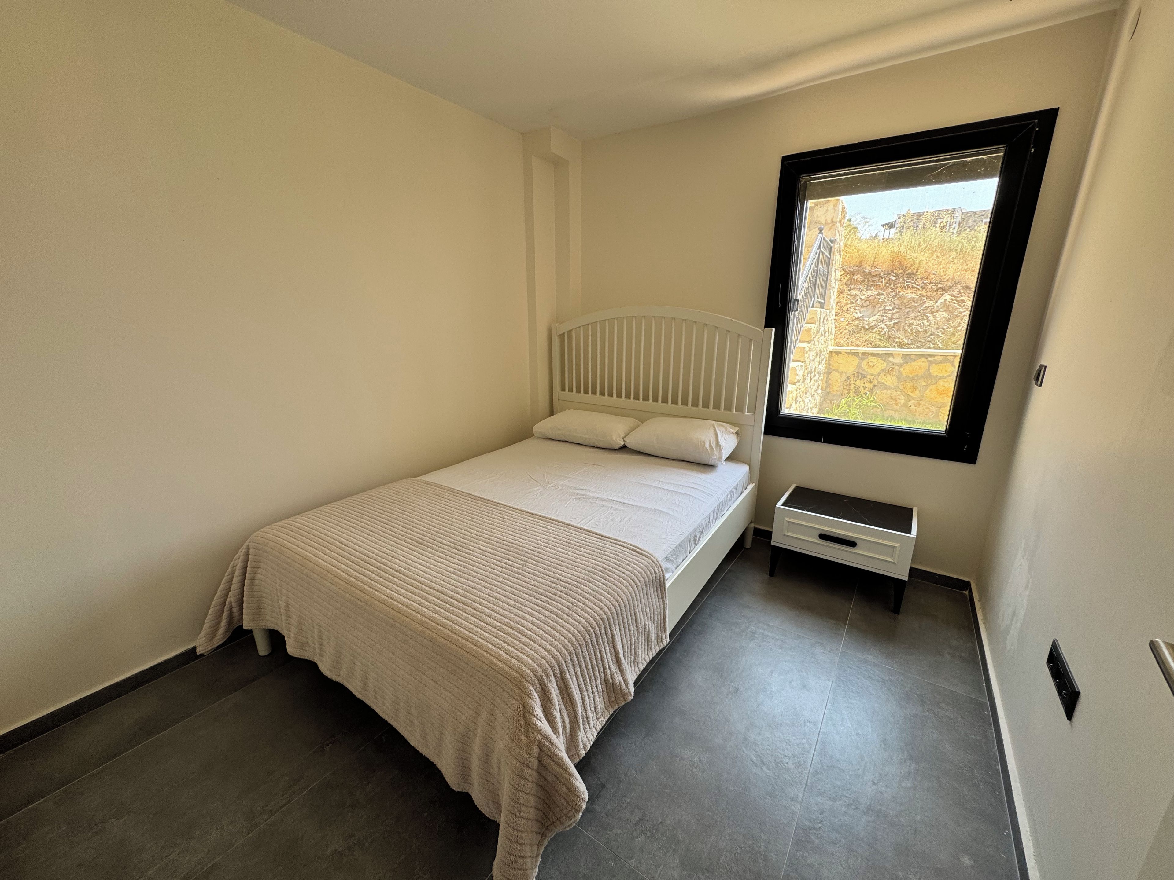 Ein Schlafzimmer mit einem Einzelbett, einem Fenster und einem kleinen Nachttisch.