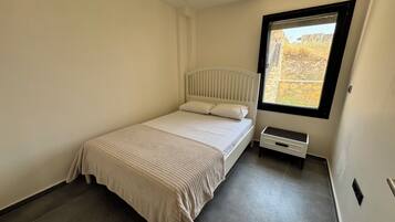 Ein Schlafzimmer mit einem Einzelbett, einem Fenster und einem kleinen Nachttisch.