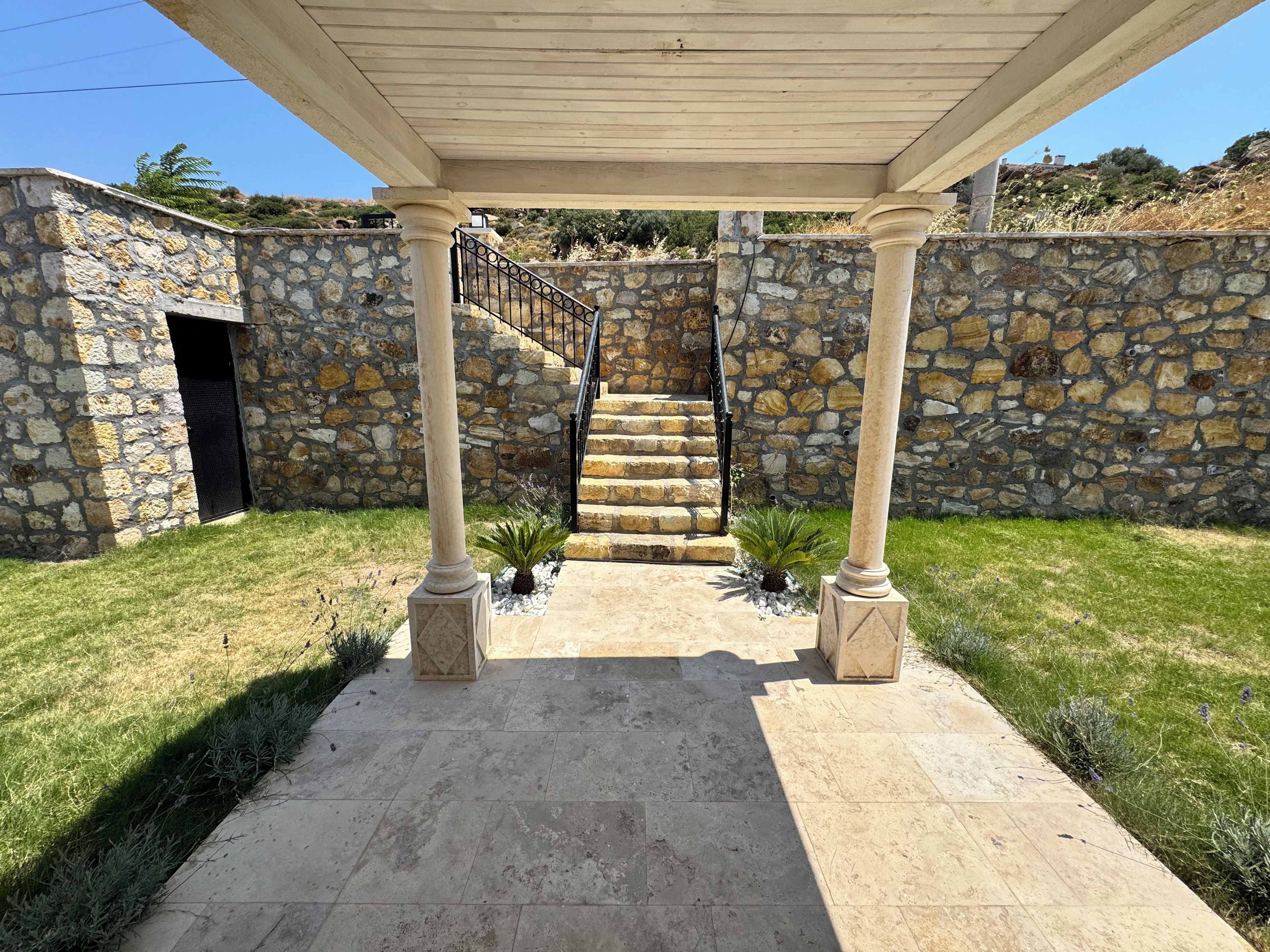 A stone-walled building with a covered entrance, a staircase, and a pergola structure.