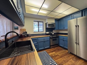 A modern kitchen with blue cabinets, stainless steel appliances, a black sink, and a window with a view of trees. - 3388 Pine Hill Road 2 Bedroom Home (South Lake Tahoe)