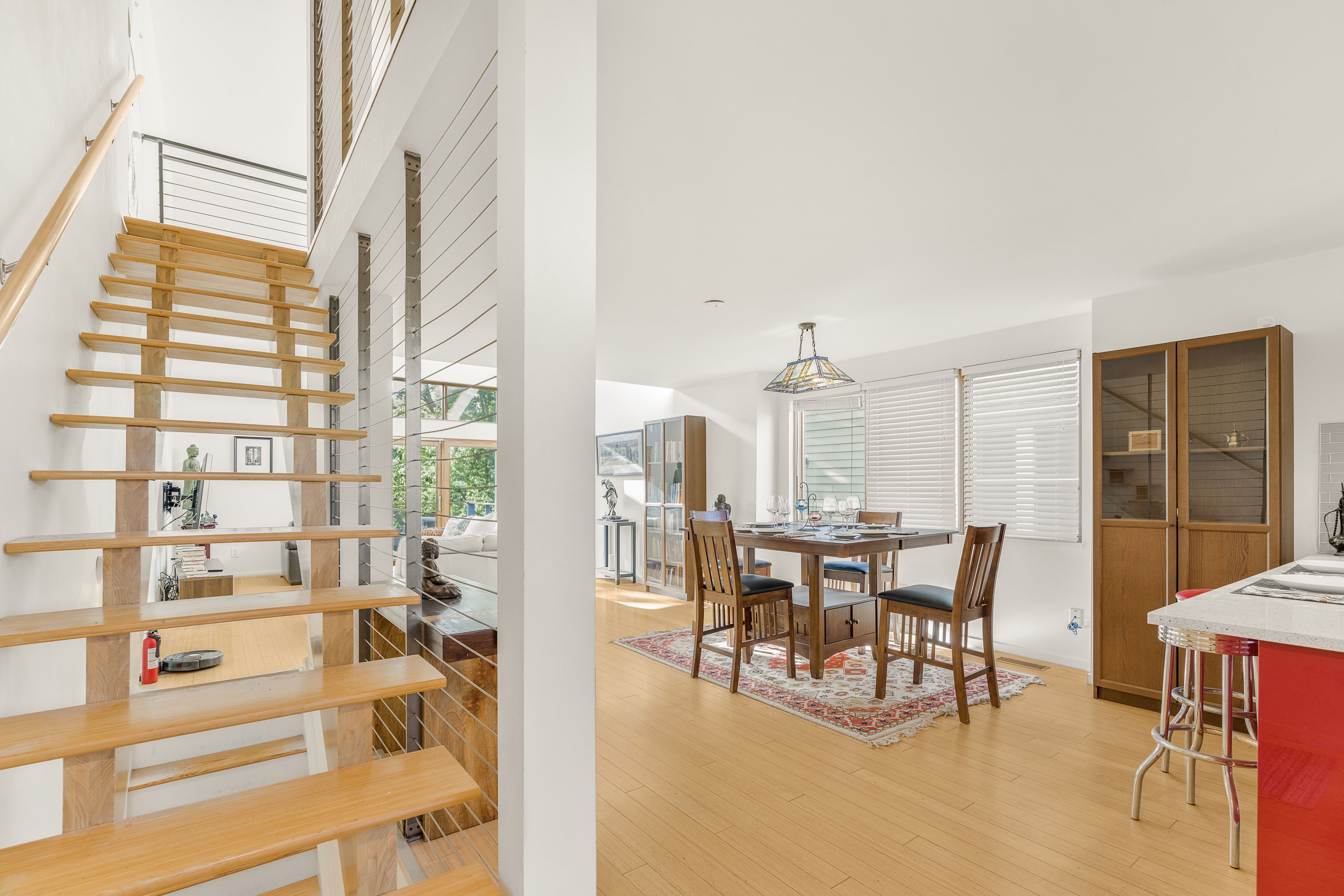 Un interior moderno con una escalera de madera, un comedor con mesa redonda y una cocina con armarios de madera.