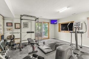 A gym with exercise equipment, a bench, a television, and a window with a view of greenery. - Relax In Charlottesville Sauna Full Home Gym 2 Bedroom Home (Charlottesville)