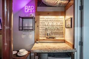 A bar area with a neon sign, a wooden wall, and a countertop with glasses and a cocktail shaker. - Relax In Charlottesville Sauna Full Home Gym 2 Bedroom Home (Charlottesville)
