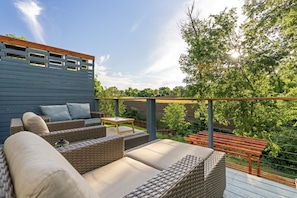 An outdoor patio with wicker furniture, a wooden table, and a view of a garden and trees. - Relax In Charlottesville Sauna Full Home Gym 2 Bedroom Home (Charlottesville)