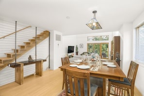 A modern dining area with a wooden table set for six, a staircase with wooden steps, and a large window with a view of greenery. - Relax In Charlottesville Sauna Full Home Gym 2 Bedroom Home (Charlottesville)