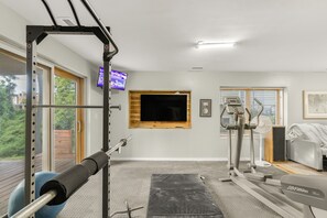 A home gym with exercise equipment, a television, and a large window. - Relax In Charlottesville Sauna Full Home Gym 2 Bedroom Home (Charlottesville)