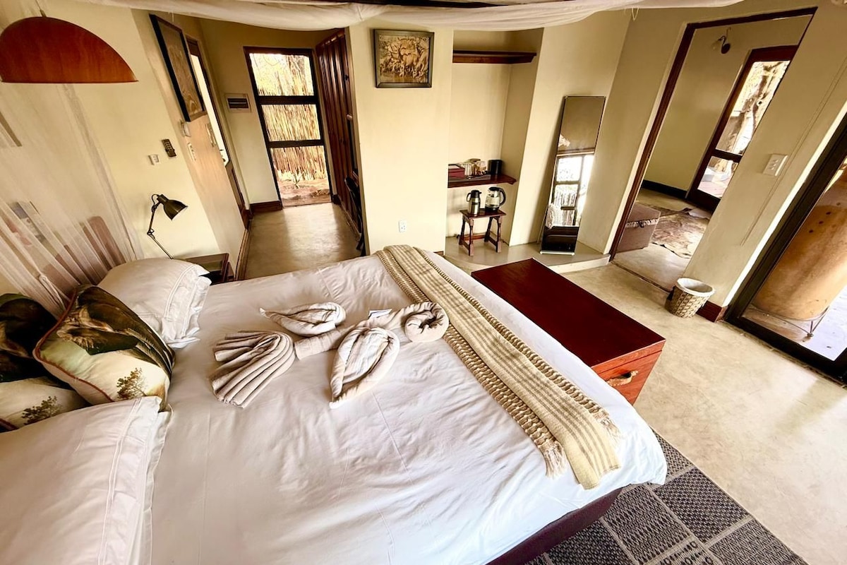 A spacious bedroom with a large bed, a bedside table, a chair, and a view of the outside.