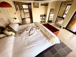 A spacious bedroom with a large bed, a bedside table, a chair, and a view of the outside.