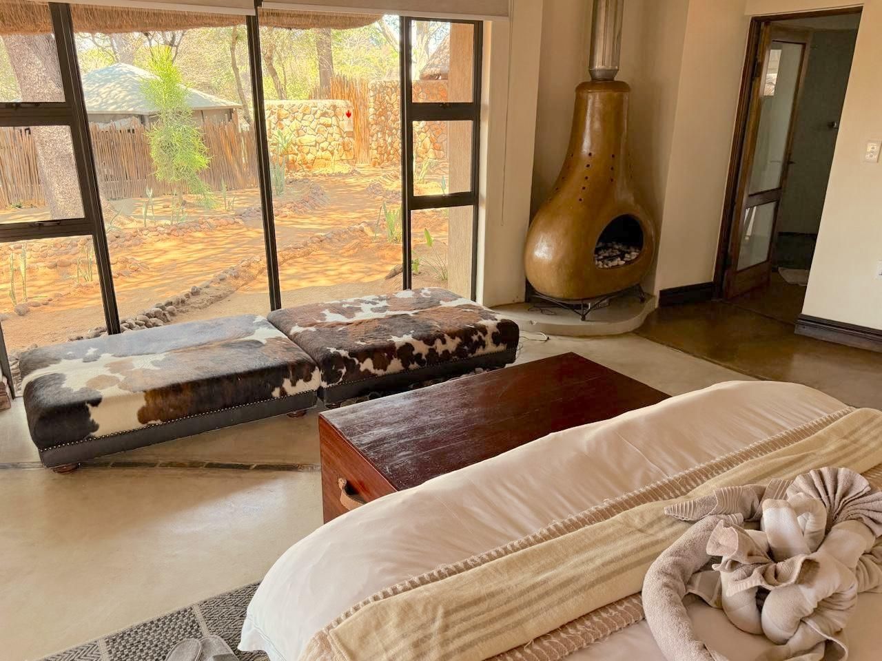 Una habitación con una cama, un banco de madera, una chimenea y vistas a un espacio exterior.