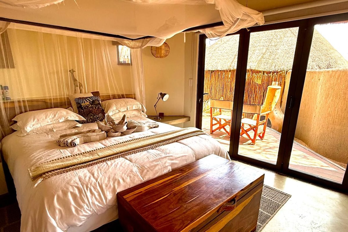 A bedroom with a bed, bedside table, and a view of an outdoor area with a chair.