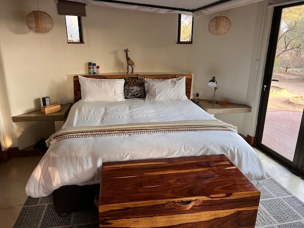 A bedroom with a large bed, bedside tables, a wooden bench, and a view through a glass door.