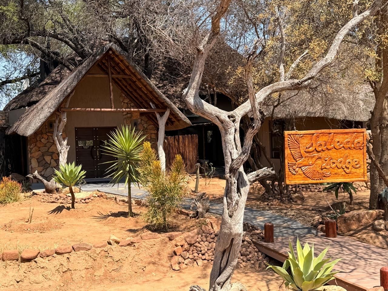 A rustic building with a thatched roof, surrounded by desert vegetation and a signboard.
