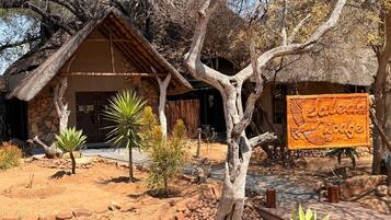 A rustic building with a thatched roof, surrounded by desert vegetation and a signboard.