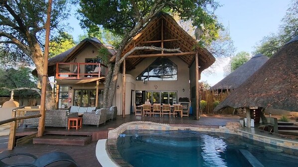 A poolside area with a hot tub, outdoor seating, and a thatched-roof structure.