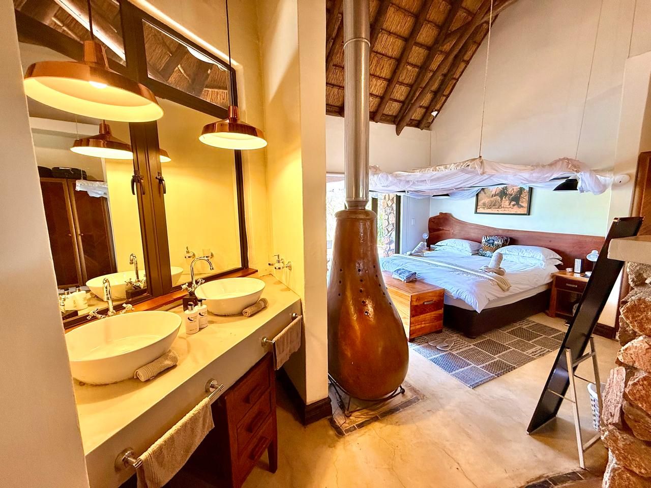 Une salle de bain avec deux lavabos et un grand miroir, une chambre avec un lit et une table de chevet, et un vase décoratif unique.