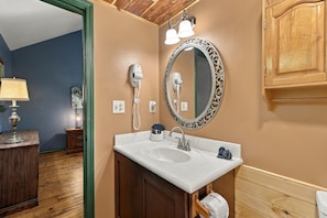 A bathroom with a wooden vanity, a white sink, a mirror with an ornate frame, and a hairdryer mounted on the wall. - Hideaway Overlook 1 Bedroom Cabin (Sevierville)