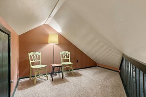 Ein kleiner, schräger Raum mit zwei Stühlen und einem Tisch, Teppichboden und einer Lampe.