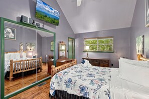A bedroom with a large mirror, a bed with floral bedding, a dresser, and a window with a view of greenery. - Hideaway Overlook 1 Bedroom Cabin (Sevierville)