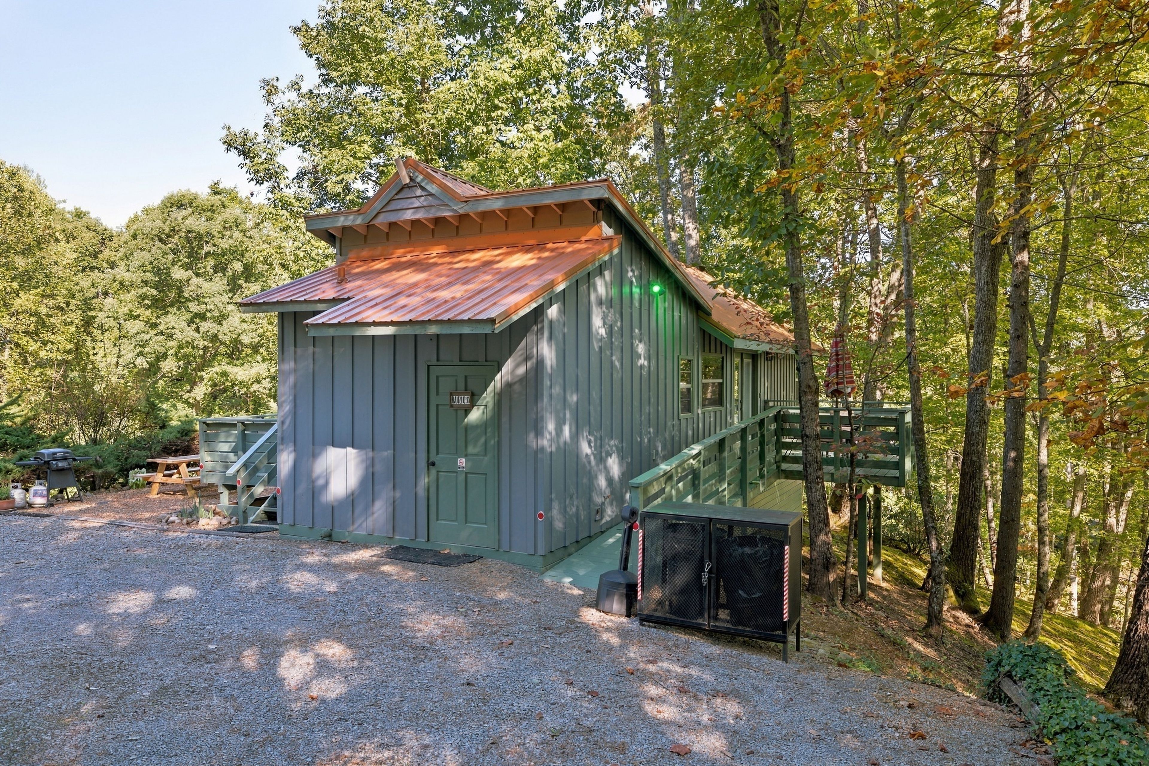 A rustic cabin with a green door, a small porch, and a gravel driveway.