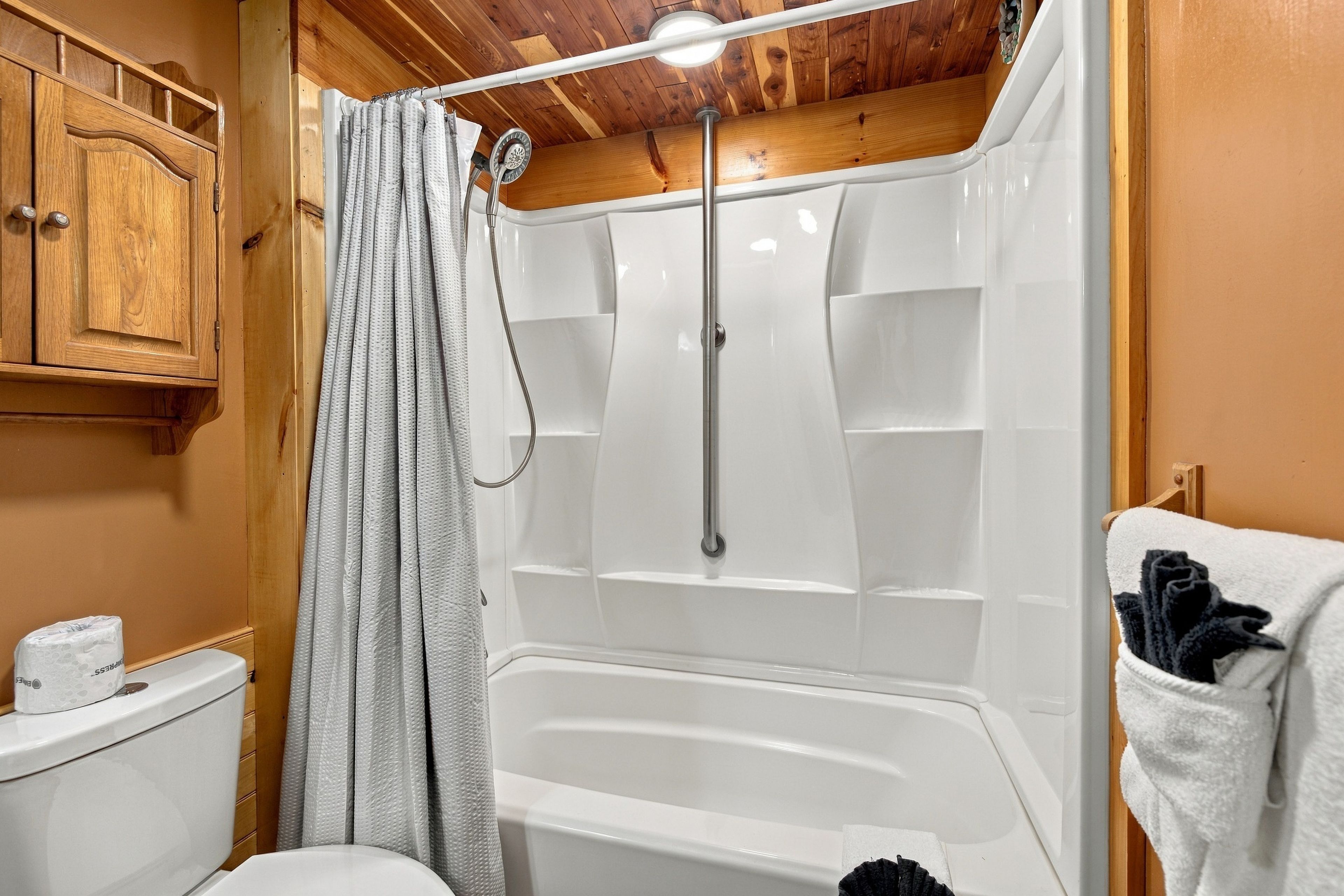 Un baño con ducha, inodoro y armarios de madera.