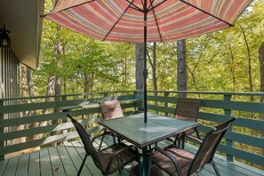 An outdoor deck with a table and chairs, a striped umbrella, and a view of a forest. - Hideaway Overlook 1 Bedroom Cabin (Sevierville)