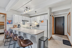Una cocina moderna con gabinetes blancos, una isla grande con taburetes de bar, un refrigerador de acero inoxidable y una cafetera.