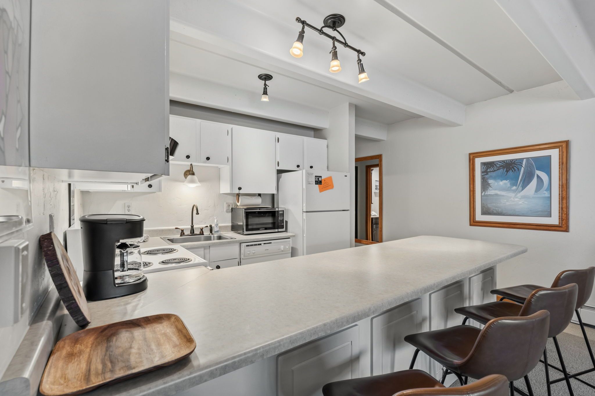Una cocina moderna con armarios blancos, una isla grande con taburetes de bar y un cuadro en la pared.