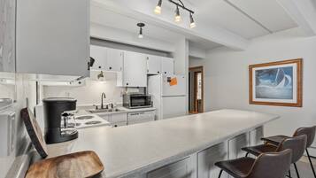Una cocina moderna con armarios blancos, una isla grande con taburetes de bar y un cuadro en la pared.