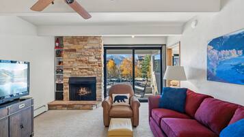 A living room with a stone fireplace, a television, a leather armchair, and a red sofa.