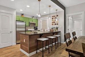 A modern kitchen with green cabinets, a stainless steel refrigerator, a microwave, and a central island with bar stools. - Premium Unit 3129 - 2 Br - Fraser Crossing 2 Bedroom Condo (Winter Park)