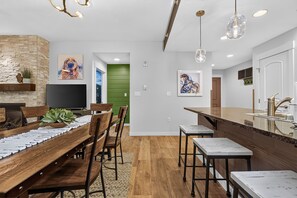 Una cocina moderna con una isla de madera, un área de comedor con una mesa larga y sillas, y una pared de acento verde.