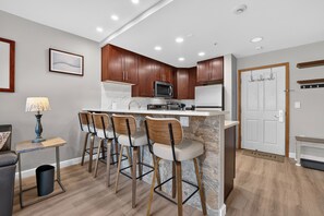 A modern kitchen with a bar area, wooden cabinets, and a stone backsplash. - Premium Unit 1320 - 1 Br - Zephyr Mountain Lodge 1 Bedroom Condo (Winter Park)