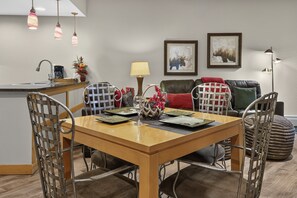 A dining area with a wooden table, metal chairs, a coffee machine, and a vase of flowers. - Premium Unit 3313 - One Bedroom w/Full Kitchen- Fraser Crossing/Founders Pointe 1 Condo (Winter Park)