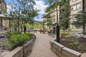 A paved walkway with benches and picnic tables, surrounded by stone planters and trees. - Premium Unit 3313 - One Bedroom w/Full Kitchen- Fraser Crossing/Founders Pointe 1 Condo (Winter Park)