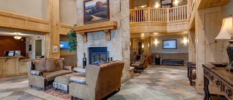 A spacious lobby with a stone fireplace, high ceilings, and a balcony overlooking the interior.