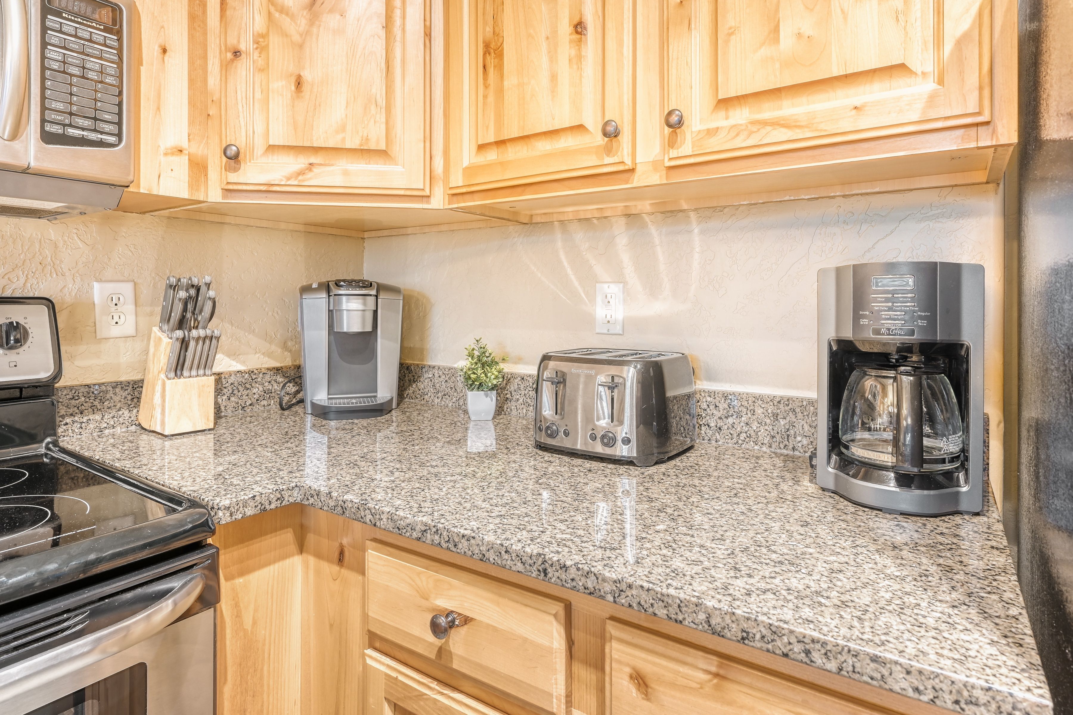 A kitchen with wooden cabinets, a coffee maker, a toaster, and a kettle.