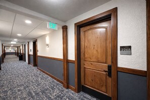 A hotel hallway with a carpeted floor, wooden doors, and an exit sign. - Heart Of Canyons Village Walk To Lifts 226 1 Bedroom Condo (Park City)