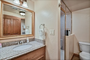 A bathroom with a granite countertop sink, a wooden vanity, a large mirror, a towel rack, a shower with a glass door, and a toilet. - Villa 3054 2 Bed 2 Bath Full Kitchen 2 Bedroom Villa (Midway)