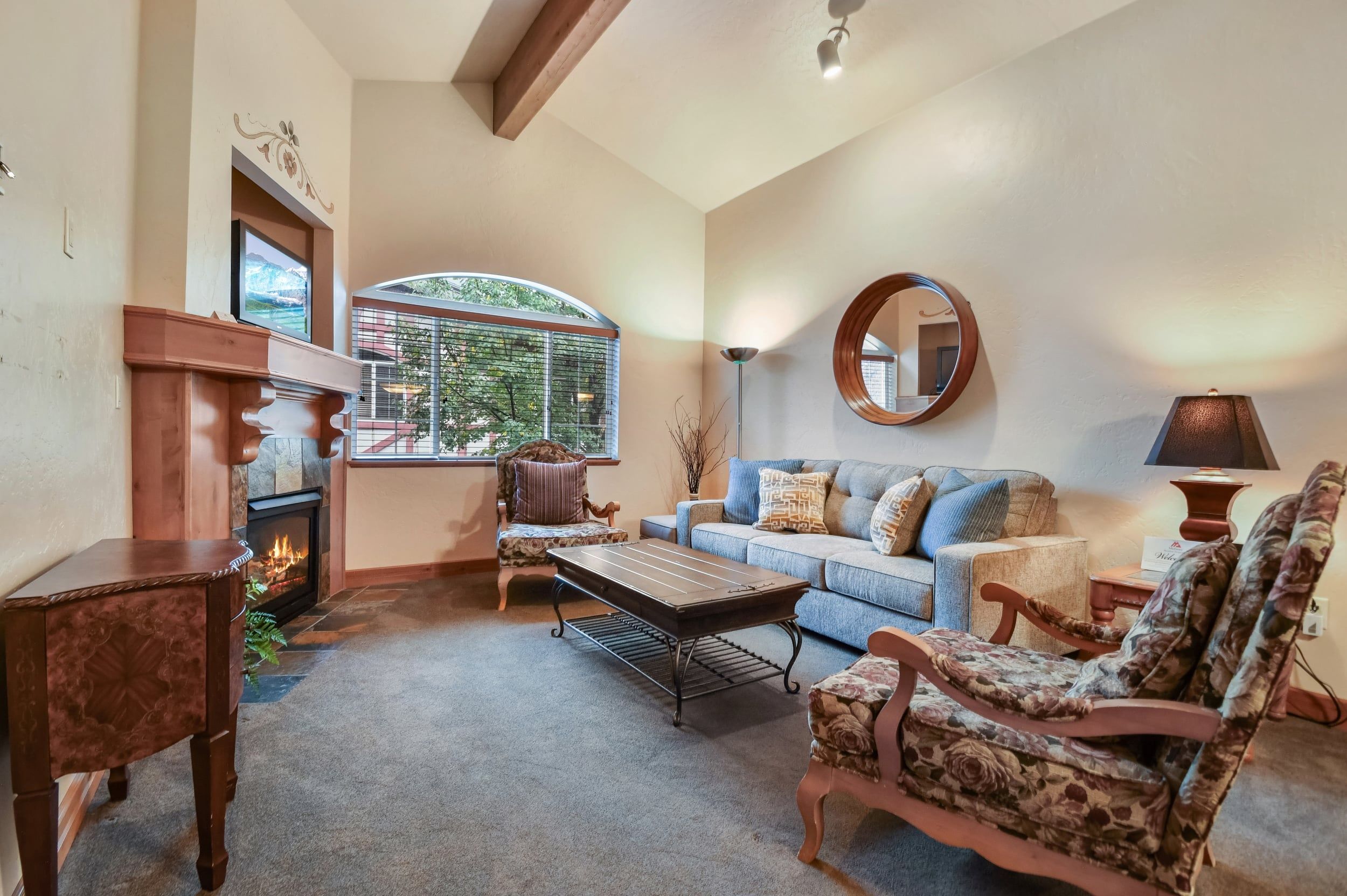 A living room with a fireplace, a sofa, a coffee table, and a large window with a view.