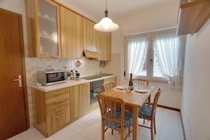 A compact kitchen with wooden cabinets, a microwave, a sink, and a dining table with chairs. - Family Garden - a 350 Dalla Spiaggia con Terrazza (Lignano Sabbiadoro)
