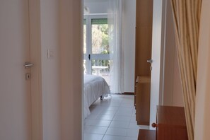 A bedroom with a bed, a wooden door, and a view of the outdoors through a window. - Family Garden - a 350 Dalla Spiaggia con Terrazza (Lignano Sabbiadoro)