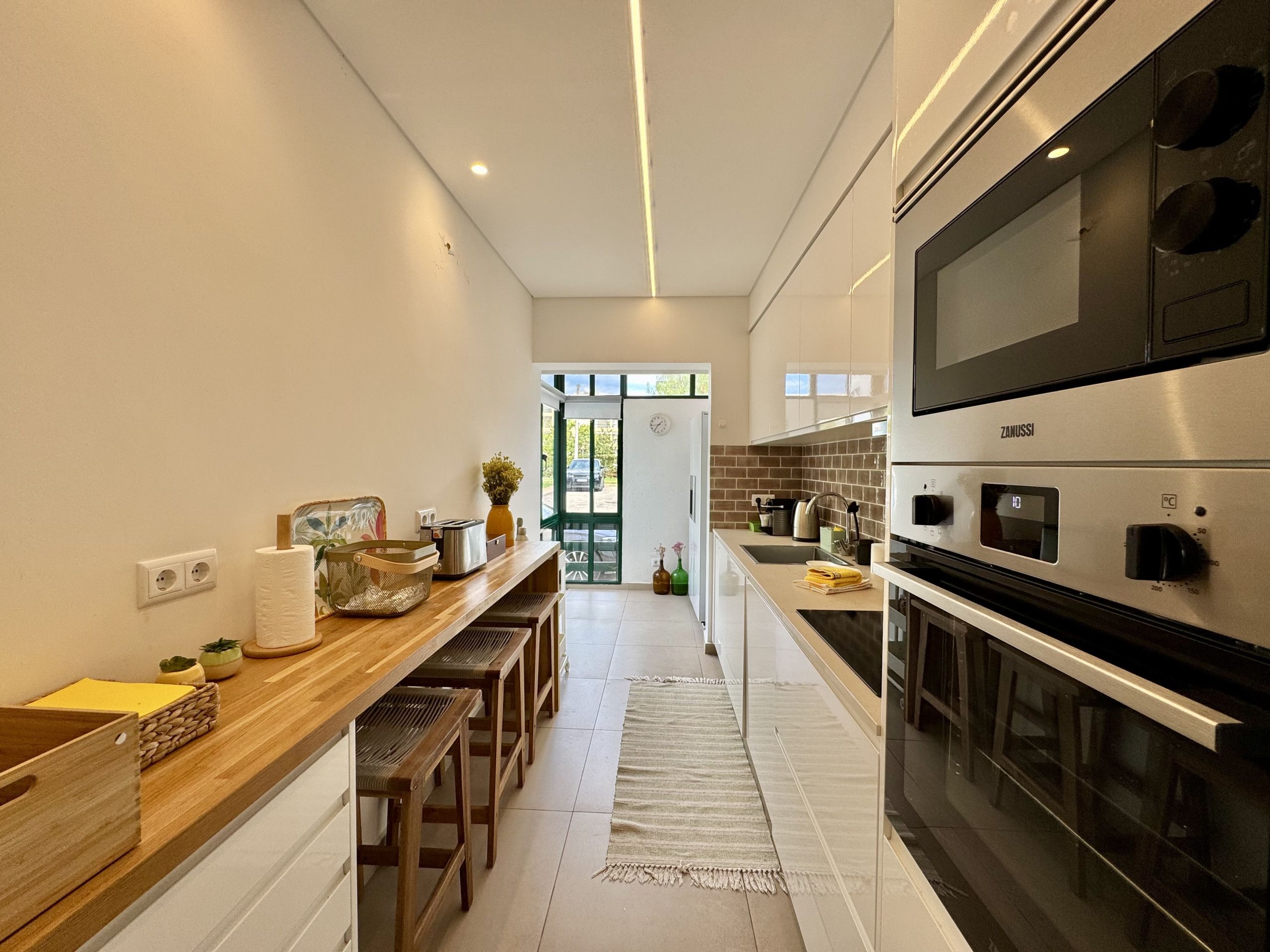 A modern kitchen with a wooden countertop, stainless steel appliances, and a view to the outside.