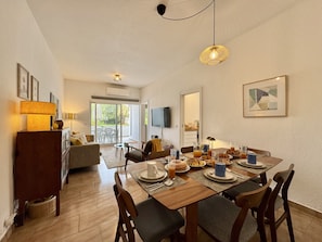 A dining area with a table set for breakfast, a sofa, and a TV mounted on the wall. - Vilamoura Downtown 3 With Pool by Homing (Loulé)