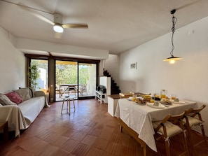 Ein geräumiger Wohnbereich mit einer Couch, einem Esstisch für zwei Personen und einer Glastür, die auf einen Balkon führt.