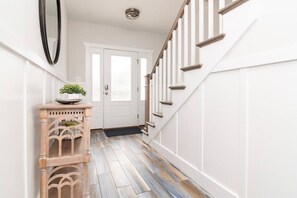A hallway with a wooden console table, a potted plant, and a staircase with white railings. - Spacious 8BR Dewey Beach Home | Private Seasonal Pool + Decks (Dewey Beach)
