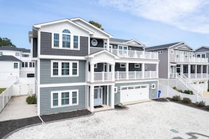 A multi-story residential building with a garage, a balcony, and a driveway. - Spacious 8BR Dewey Beach Home | Private Seasonal Pool + Decks (Dewey Beach)