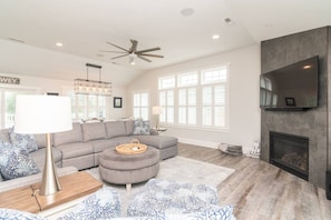 A modern living room with a sectional sofa, ottoman, and a fireplace. - Spacious 8BR Dewey Beach Home | Private Seasonal Pool + Decks (Dewey Beach)